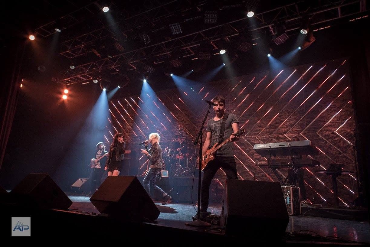 The band on a large stage under rows of moving lights