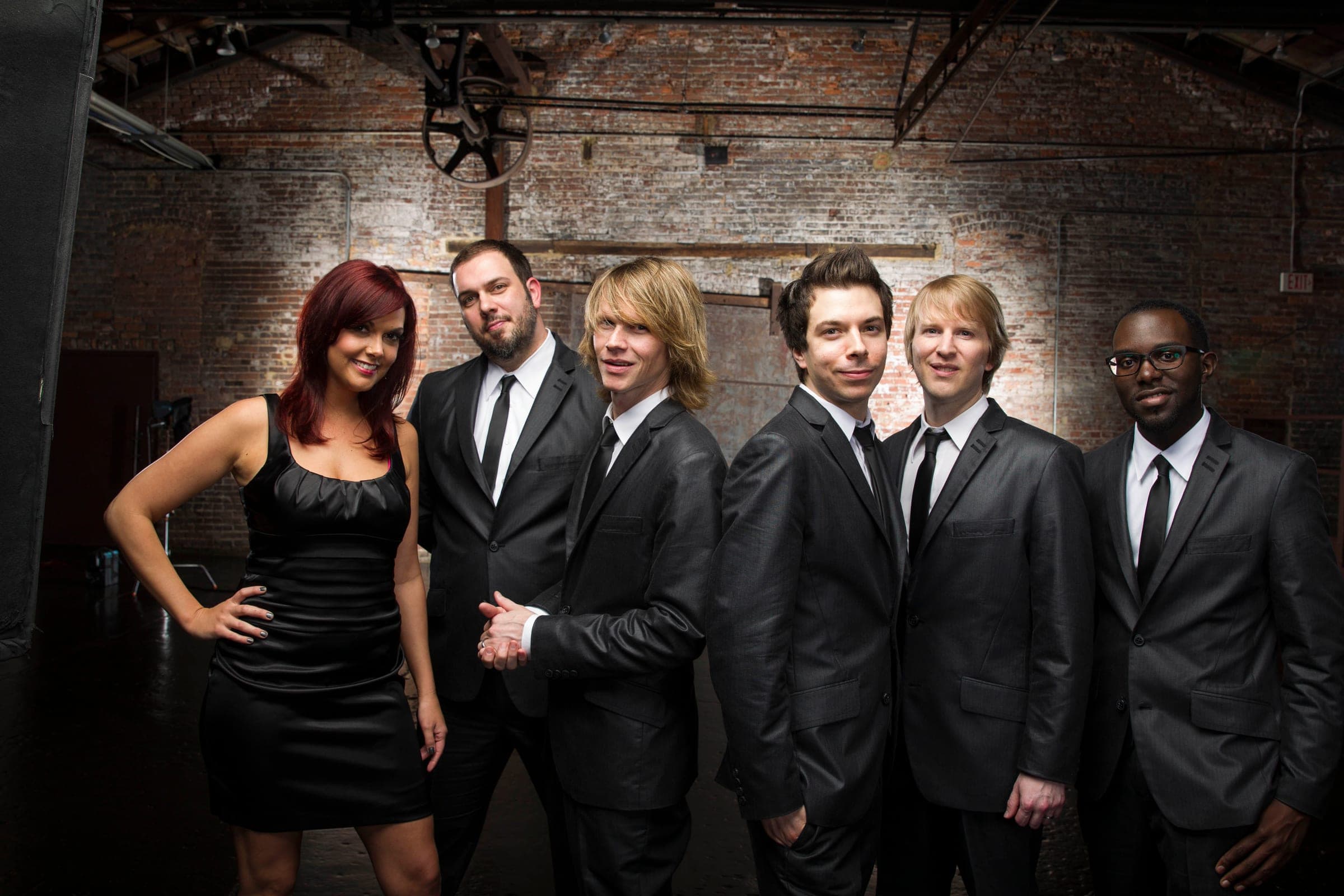 The band in black suits and a black dress against a brick wall