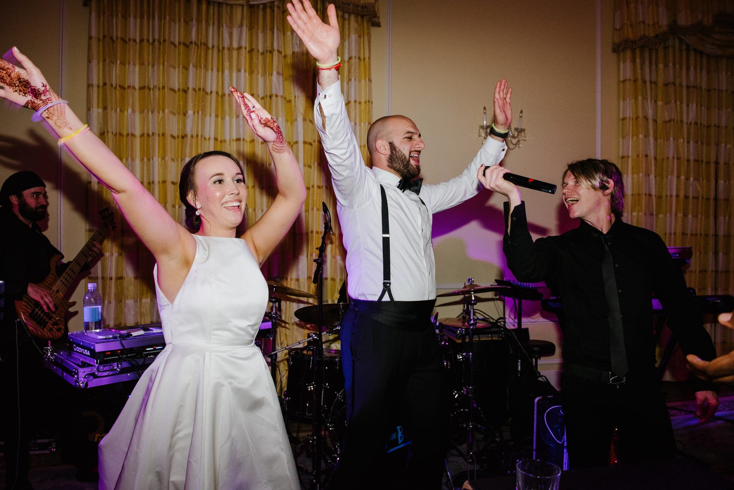 A bride and the band's singer with their arms raised, mid-song