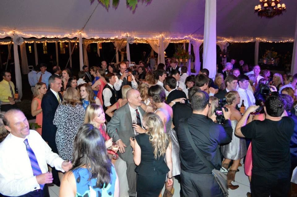 A tented wedding reception with the dance floor full of guests